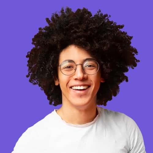 Teen male smiling with brown hair sticking up and wearing glasses with a blue background.